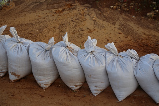 Line of white sandbags, sacks  full of sand on the brown - orange soil. 