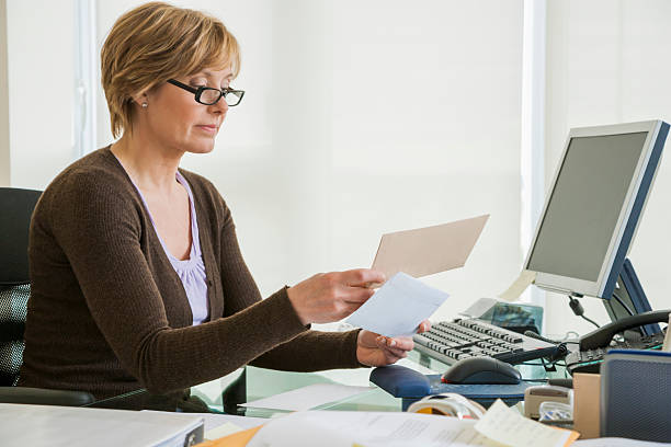 frau mittleren alters, die rechnungen am computer betrachtet - opening mail letter envelope stock-fotos und bilder