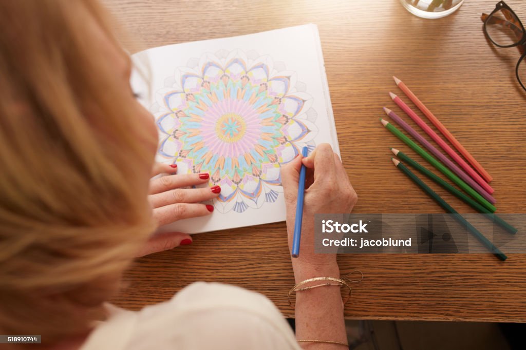 Drawing in adult coloring book Overhead view of woman drawing in adult coloring book with color pencils. Anti stress exercise at home. Coloring Stock Photo