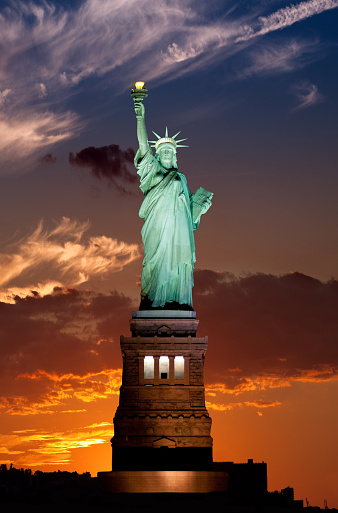 Sunset scene of the illuminated Statue of Liberty. Vivid blue and red sky with clouds is in background. The Statue of Liberty is on Liberty Island in the middle of New York Harbor, in Manhattan, New York City.
