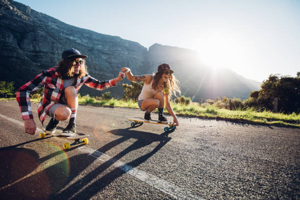 pareja divirtiéndose con monopatín en la calle - patinaje en tabla larga fotografías e imágenes de stock