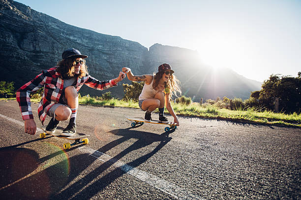Couple having fun with skateboard on the road Happy young couple having fun with skateboard on the road. Young man and woman skating together on a sunny day. longboard skating photos stock pictures, royalty-free photos & images