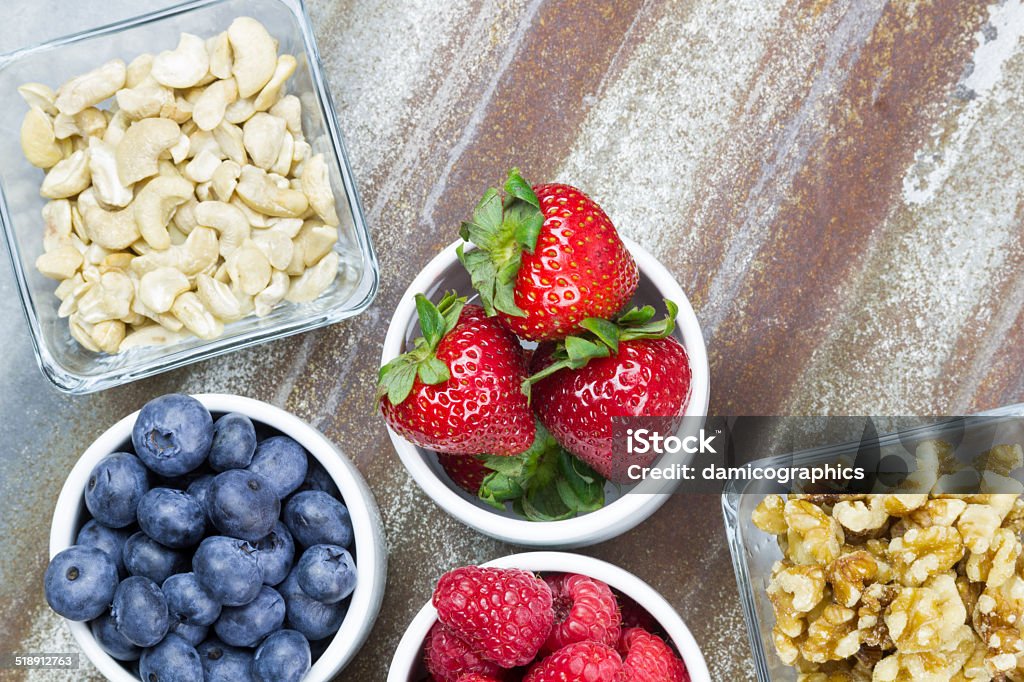 Healthy snack foods of berries and nuts Small portion bowls of raspberries, blueberries, strawberries, cashews and walnuts with rustic background, horizontal layout, bird eye view Antioxidant Stock Photo