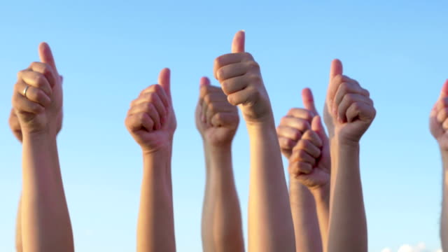 Hands with thumbs up raised against blue sky
