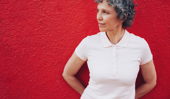 Portrait of mature woman standing against red background and looking away at copy space.