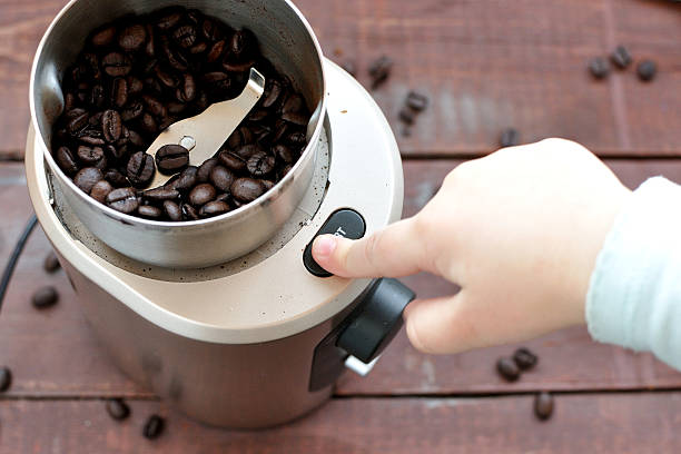 Baby's hand reaching start button of electric coffee grinder stock photo