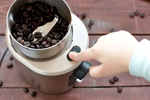 Baby's hand reaching start button of electric coffee grinder. Selective focus