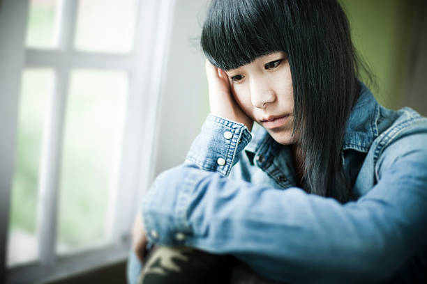 Asian teenager girl sitting near window with sadness. stock photo