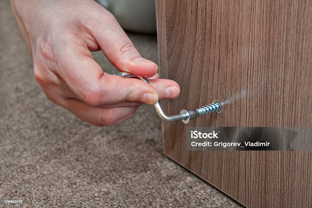 Hex wrench, Allen Key, human hand makes screwed furniture screw. Hex wrench, Allen Key close-up of human hand assembling furniture at home. Allen - Texas Stock Photo