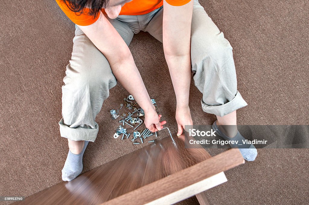 One Caucasian woman assembles furniture at home using Allen key Caucasian woman housewife mounts wooden furniture at home. Adult Stock Photo