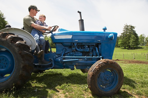 Father and son riding tractor on farm