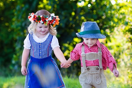 Kids in traditional Bavarian costumes in wheat field. German children eating bread and pretzel during Beer Fest in Munich. Brother and sister play outdoors during autumn harvest time in Germany.