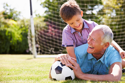 Portrait Of Grandfather And Grandson With Football Lying On The Grass Laughing