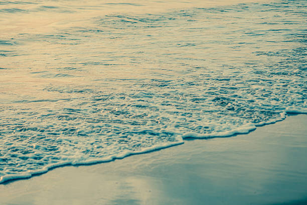 Seascape with restless pink water from sunlight and wet sand. The sea before the storm at dusk already shows small waves with sea foam at the ends.