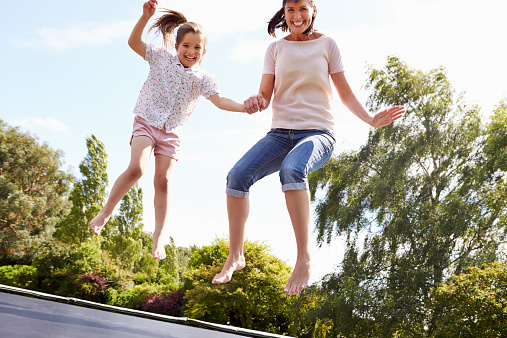 Mother And Daughter Bouncing On Trampoline Together Smiling