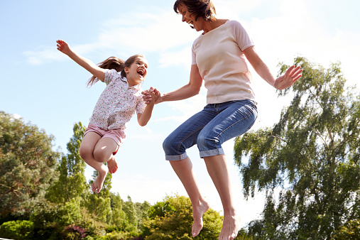 Mother And Daughter Bouncing On Trampoline Together Laughing