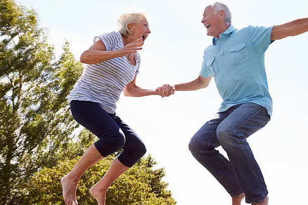 Senior Couple Bouncing On Trampoline In Garden Laughing