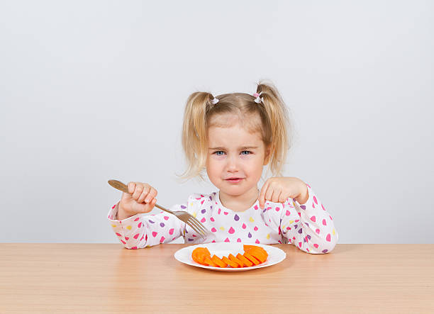 mała dziewczynka jedzenie marchew z widelec. - cute disgust carrot caucasian zdjęcia i obrazy z banku zdjęć