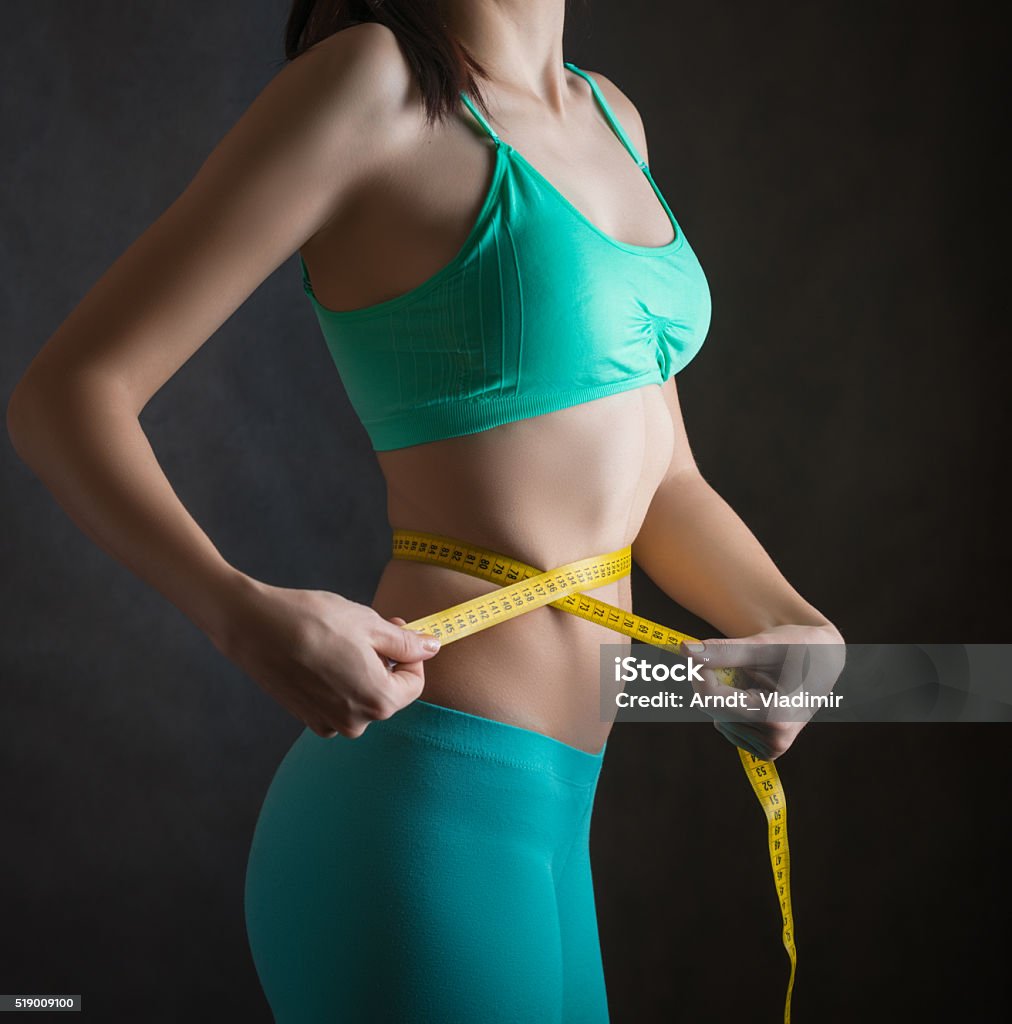 Fit and healthy young woman. Fit and healthy young woman measuring her waist with a tape measure. Adult Stock Photo