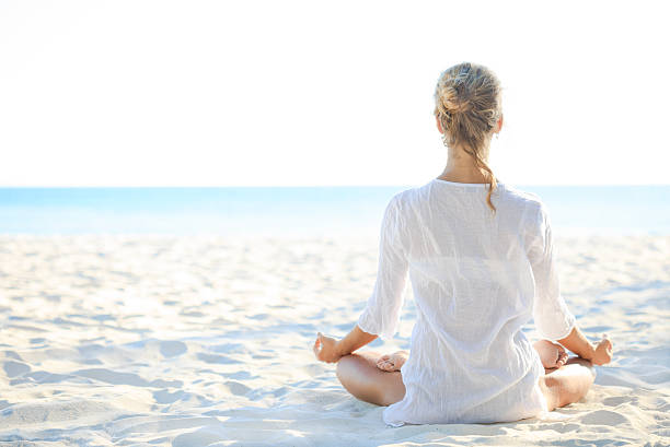 młoda kobieta siedzi na plaży i medytacji - zen like nature breathing exercise sitting zdjęcia i obrazy z banku zdjęć