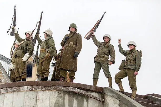 Stock photograph of WWII platoon with rifles raised after taking a bunker during a fierce battle in a blizzard.