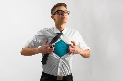 Young businessman showing suit of super hero with copy space under his shirt and tie on gray background