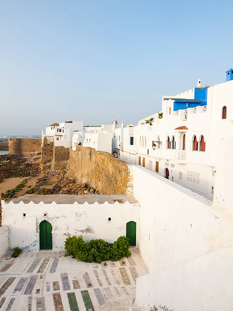 Asilah, Morocco - July 9, 2010: White walls and buildings with blue and green accents decorate the seaside city of Asilah, Morocco. People can be seen sitting by the walls.