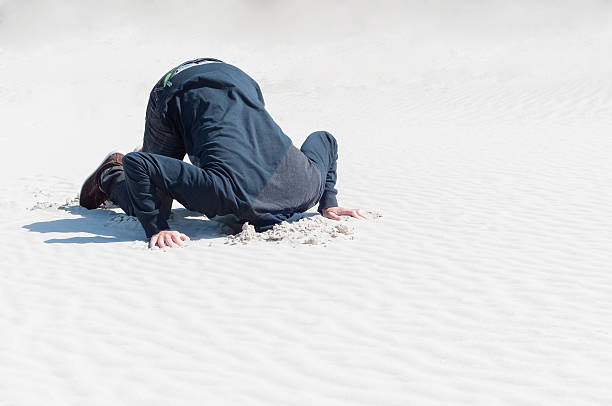 Young male hiding head in sand stock photo