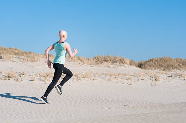 young woman with bald head jogging after chemotherapy stock photo