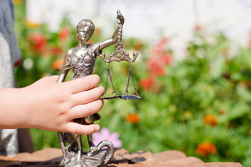 Kid's hand holding sculpture of themis, femida or justice goddess on green leaves natural bokeh background