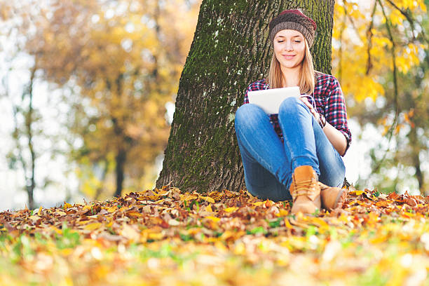 Beautiful young girl with tablet PC enjoying autumn stock photo