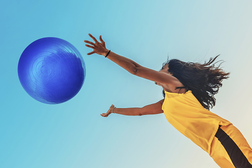 brazilian sportswoman in yellow shirt jumping for  blue big ball 