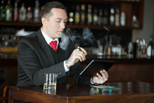Front view of businessman with scotch and cigar, using digital tablet