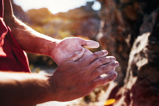 Detail of bouldering man's hands rubbing chalk in preparation for rock climbing ascent.
