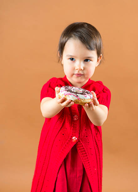 Pretty little girl holding donuts at brown background in studio