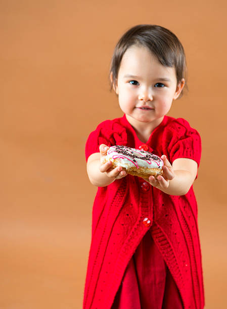 Pretty little girl holding donuts at brown background in studio