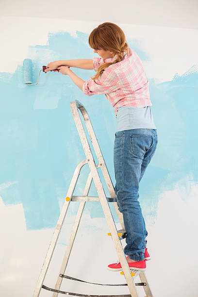 istock Woman on ladder painting wall with paint roller 519053243