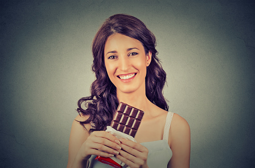 Portrait of a young brunette chocolate loving woman isolated on gray wall background. Positive human face expression. Diet concept