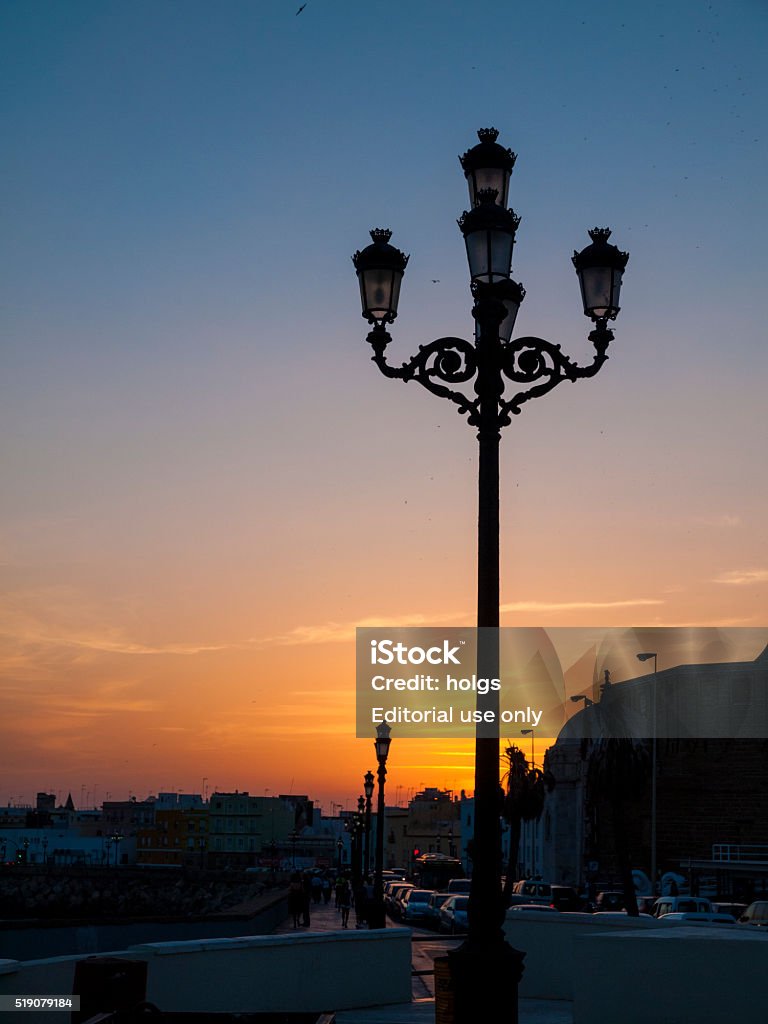 Sunset over Cadiz, Spain Cadiz, Spain - July 5, 2010: Silhouette of a street lamp in Cadiz, Spain during sunset. Cars and city buildings can be seen in the background. Back Lit Stock Photo