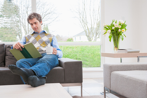 Man reading book on sofa with feet up
