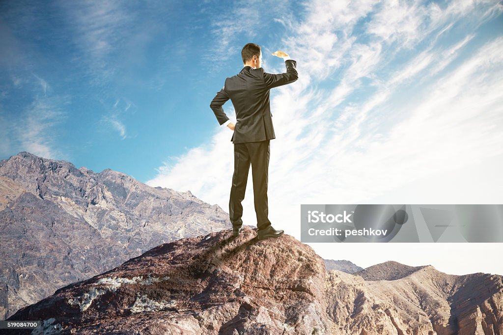 Research concept on mountain Research concept with businessman standing on mountain top, looking into the distance on clear sky background Distant Stock Photo