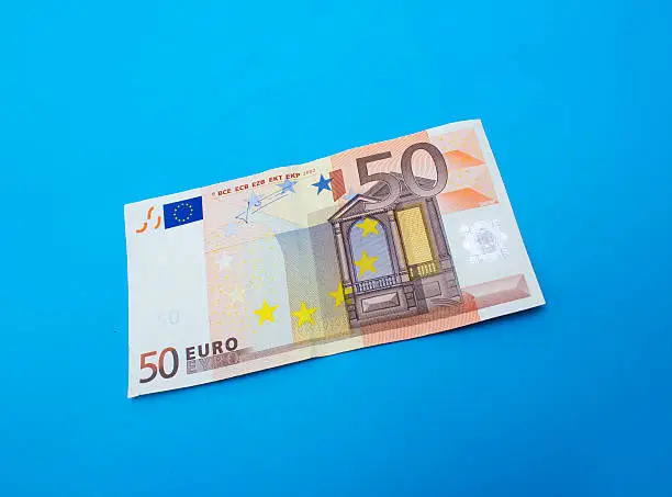 High angle view of single fifty euro banknote over blue background. Horizontal composition. Image taken in studio over isolated on blue and developed from RAW format.