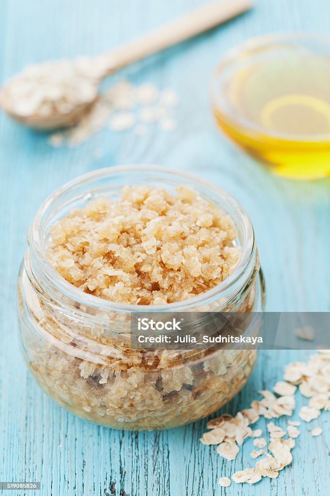 Homemade cosmetic for peeling and spa care, body scrub Body scrub of oatmeal, sugar, honey and oil in glass jar on blue rustic table, homemade cosmetic for peeling and spa care Exfoliation Stock Photo