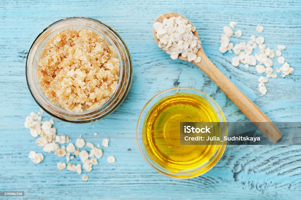 Body scrub of oatmeal, sugar, honey and oil, top view Body scrub of oatmeal, sugar, honey and oil in glass jar on blue rustic table, homemade cosmetic for peeling and spa care, top view Exfoliation Stock Photo