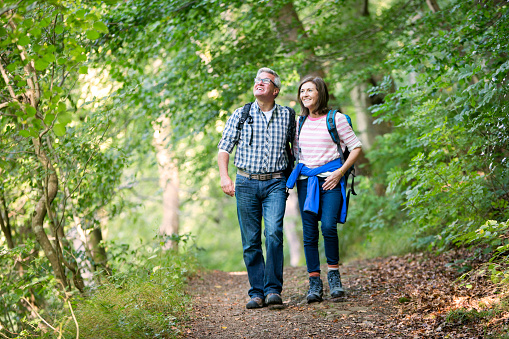 A couple are walking in a woodland area, They are looking up and smiling.