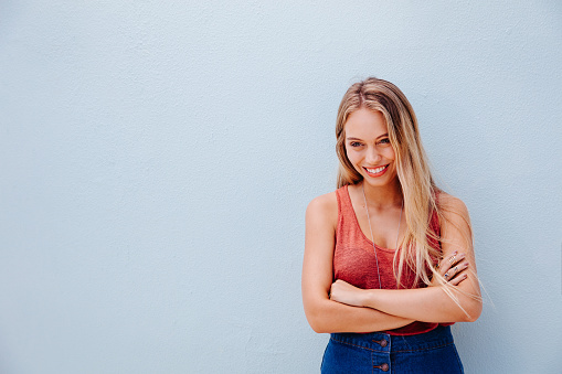 Young confident woman with crossed arms posing, isolated on blue wall background