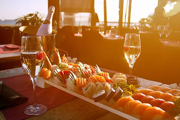 Luxury Restaurant table with sushi plate,champagne bottle  and the Barcelona beach on background. Sun flare effect .