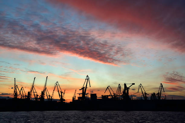 silhouette de port de grues dans le ciel coucher de soleil en arrière-plan - factory night skyline sky photos et images de collection