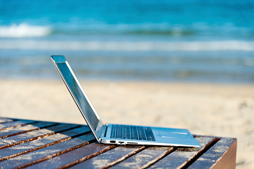 Laptop alone on empty oceanfront beach chair.