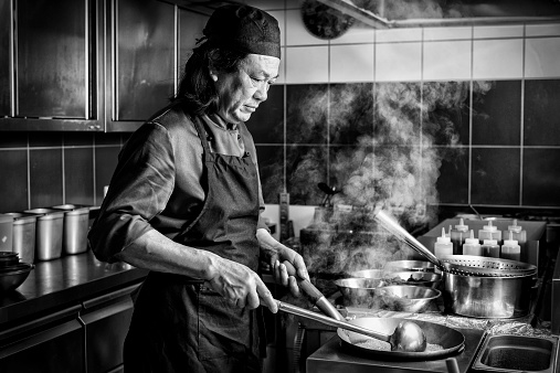 serious chinese man cooking in the kitchen of an asian restaurant